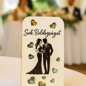 Fa esküvői pénzátadó doboz lézergravírozott „Sok Boldogságot” felirattal, szerelmespár motívummal és szív alakú áttörésekkel, esküvői háttérben