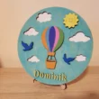 1_result Egyedi hőlégballonos gyerekszoba névtábla "Dominik" névvel, egy fa állványon elhelyezve.