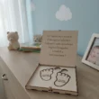 Keresztszülő felkérő ajándékdoboz egy babaszoba komódján, mackó és képkeret mellett.
