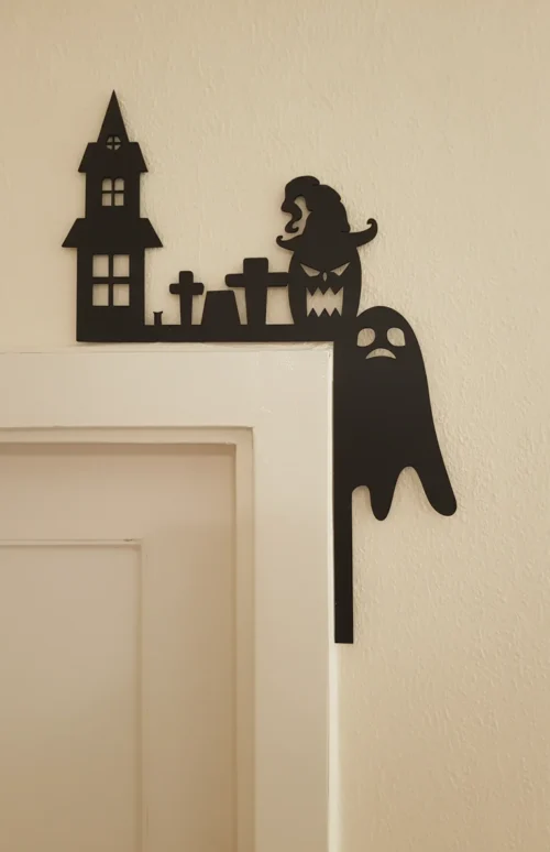 Szellem-tökfej_result Fekete halloweeni dekoráció egy ajtó sarkán, amely egy kísértetkastélyt és egy szellemet ábrázol.