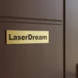 ajton3_result Arany színű ajtónévtábla egy barna fa ajtón, "LaserDream" felirattal.