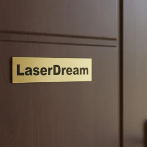 ajton3_result Arany színű ajtónévtábla egy barna fa ajtón, "LaserDream" felirattal.